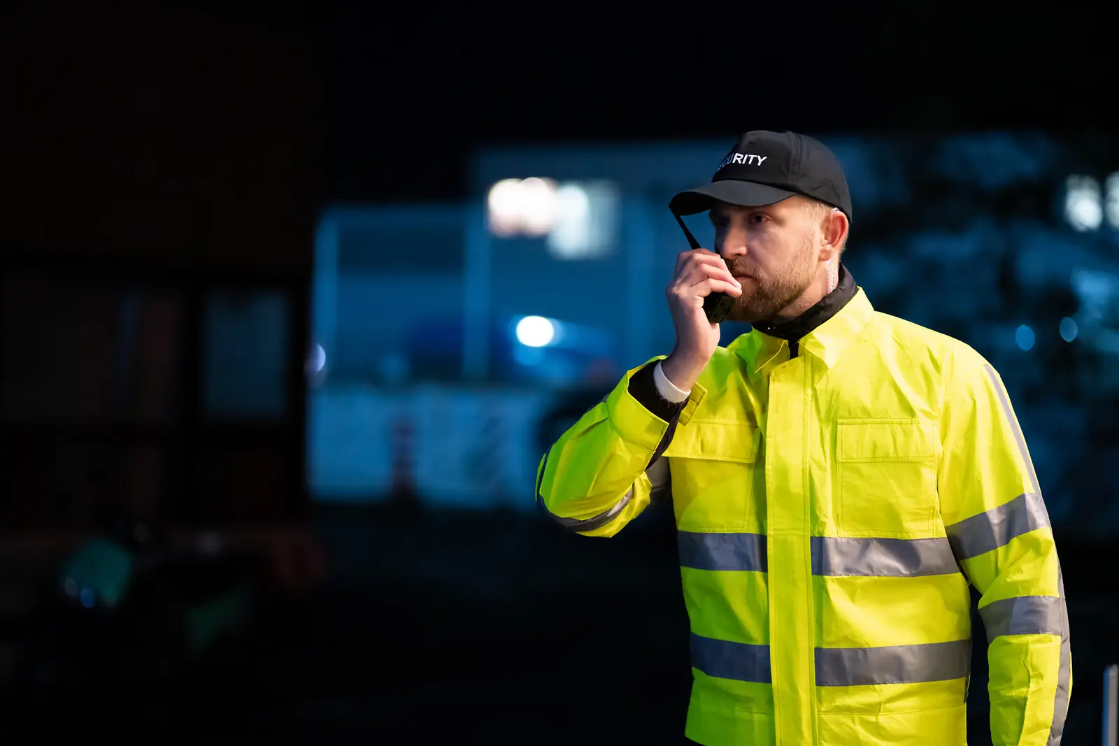 Sicherheitsmitarbeiter in Warnweste mit Funkgerät bei Nacht